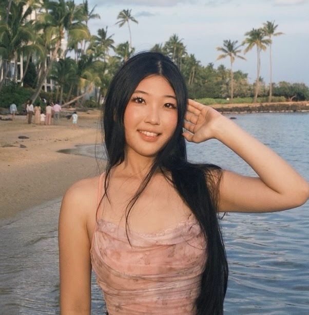 Keiko Shinha, founder of the Common Ground Foundation, on a beach in Hawaiʻi with palm trees behind her